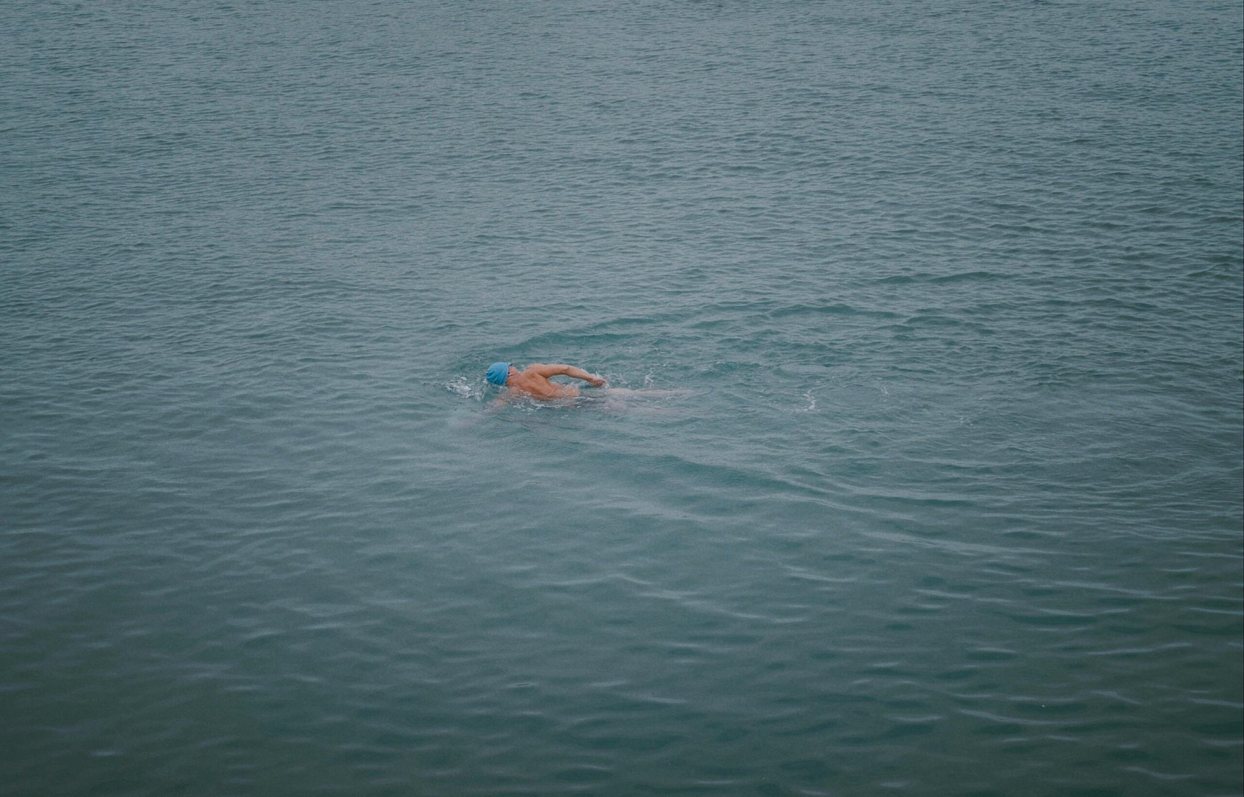 A male swimmer in a blue cap swims in open water, competing in a race.
