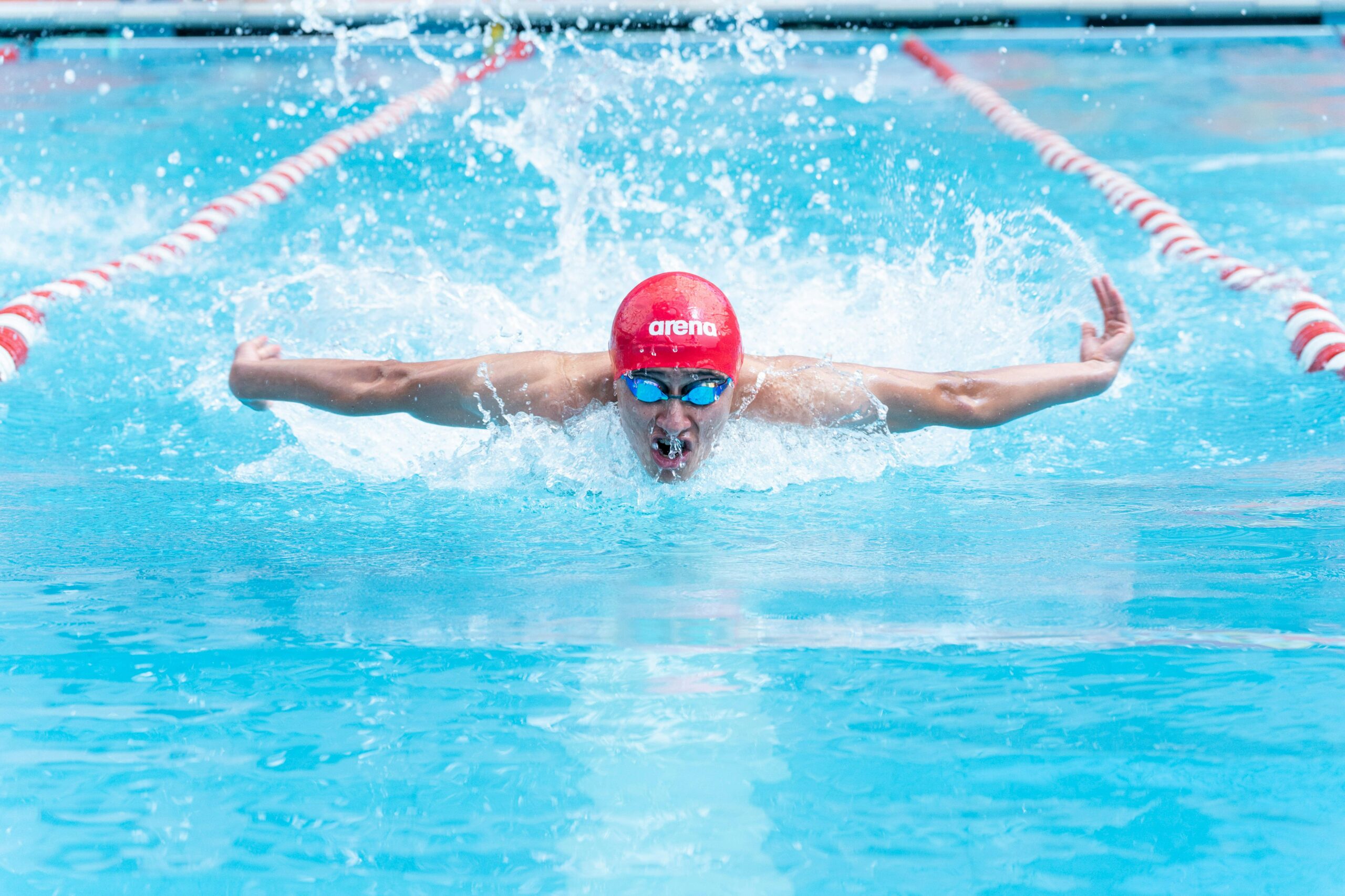A skilled swimmer performing the butterfly stroke in an outdoor pool, showcasing athletic prowess and energy.